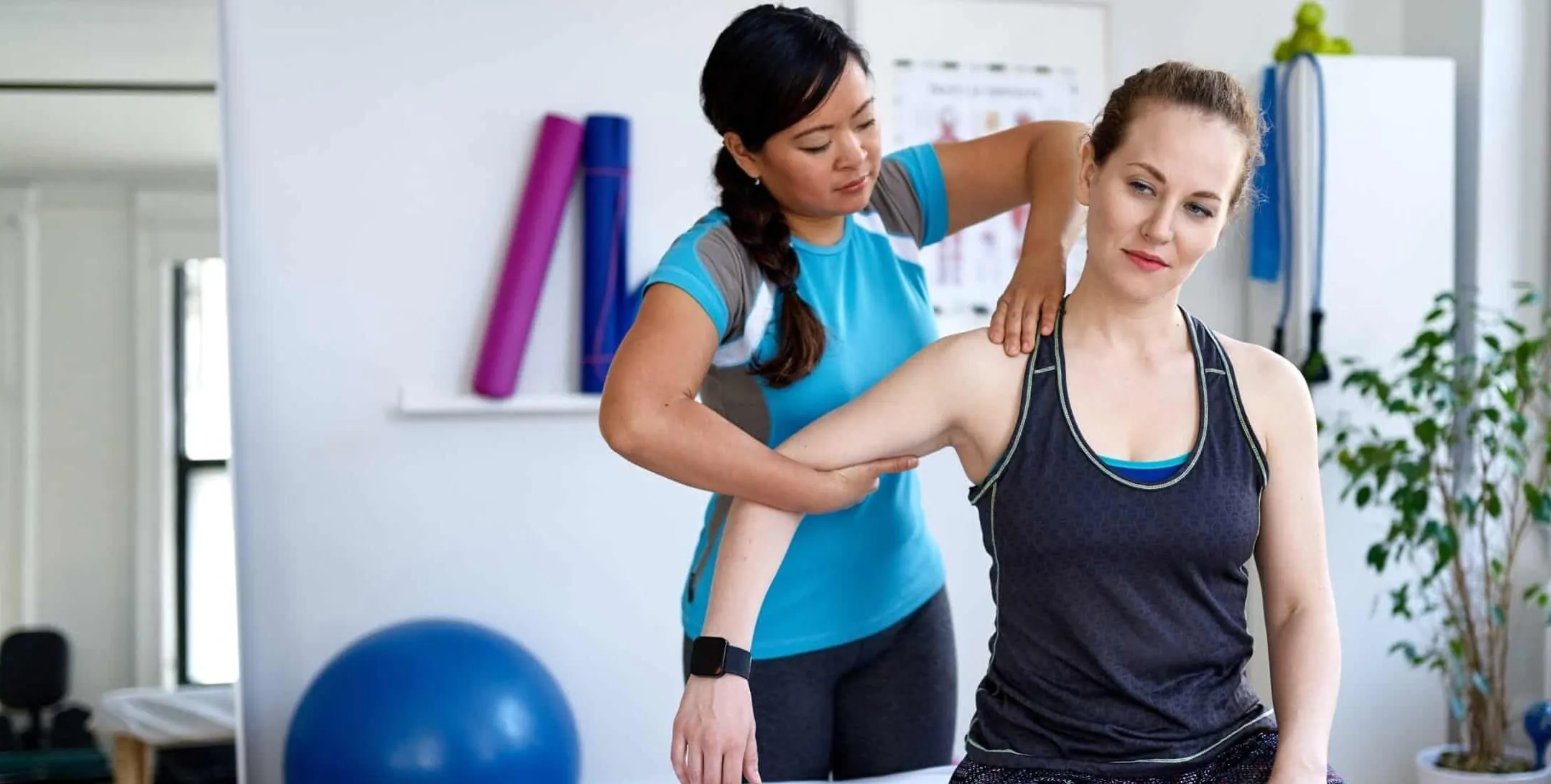 Candid image of an attractive patient during a appointment with professional asian physiotherapist in design kinesio clinic working and massaging her neck and shoulder pain